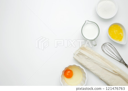 Near baking dish with ingredients, phyllo dough, egg, butter, nuts, and milk on a white background for baking Crinkle Cake 121476763