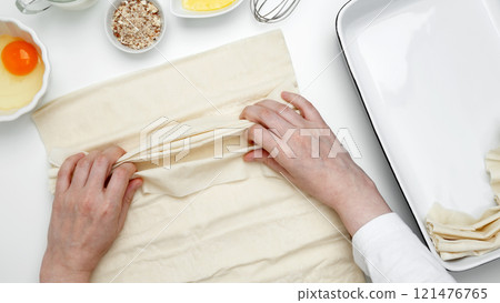 Baking Crinkle Cake. Hands folding phyllo dough with egg, butter, nuts, and milk 121476765