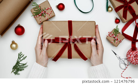 Festive decorations in a cozy holiday setting, womans hands wrapping Christmas gifts 121476796