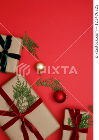Thuja branches, gifts wrapped in craft paper, Christmas ornaments arranged on a red background 121476825
