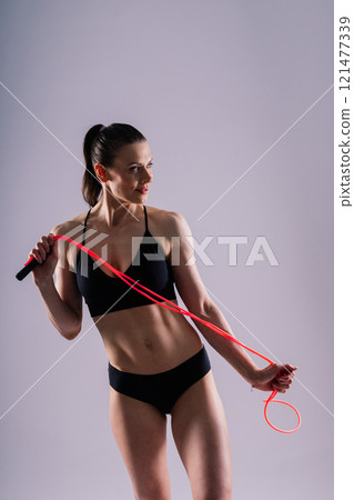 Fitness woman doing jumping exercises with skipping rope on colorful yellow red background. 121477339