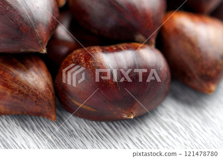 Group of fresh whole chestnuts with glossy nut shells arranged on a gray textured surface. Close up 121478780
