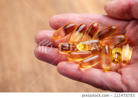 Translucent Omega-3 capsules in hand with dry wrinkled skin on a natural wooden background. Healthy supplement. Close up Translucent Omega-3 capsules in hand with dry wrinkled skin on a natural wooden background. Healthy supplement. Close up 121478783