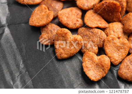 Heart shaped crunchy cat treat pieces scattered on a sleek black textured surface. Dry pet food snacks. Close up 121478787