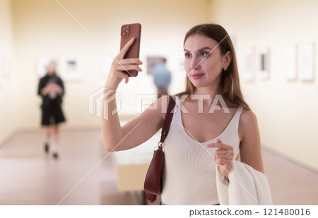Woman photographs attractive and unusual exhibit, picture and work of applied art. 121480016