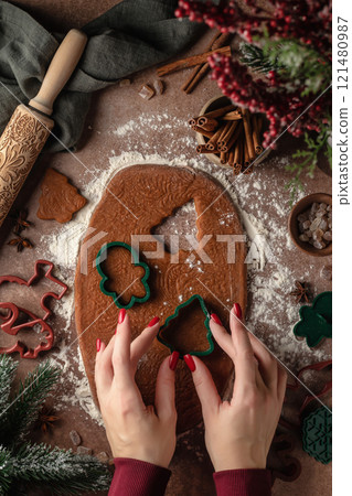 Christmas baking. Female hands cut out cookies from the dough. Ingredients for baking gingerbread. Top view 121480987