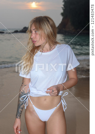 A Woman Dressed in Elegant White Swimwear Embracing the Beauty of Sunset Beach Serenity A Woman Dressed in Elegant White Swimwear Embracing the Beauty of Sunset Beach Serenity 121483478