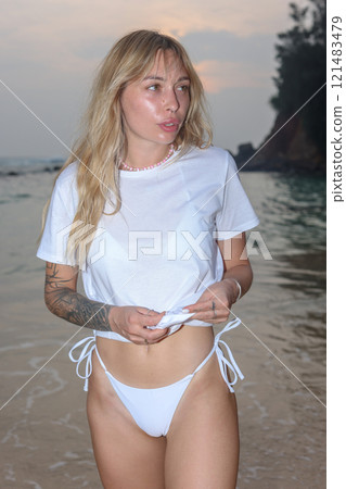 A Woman Dressed in Elegant White Swimwear Embracing the Beauty of Sunset Beach Serenity 121483479