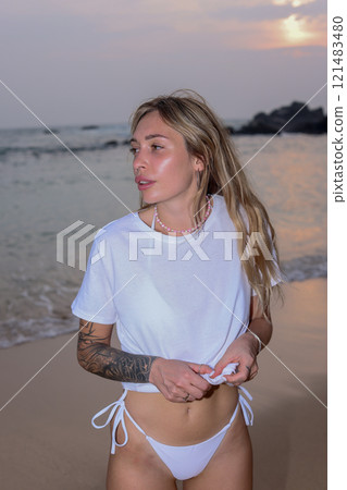 A Woman Dressed in Elegant White Swimwear Embracing the Beauty of Sunset Beach Serenity 121483480