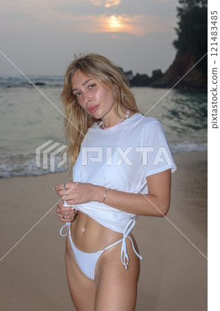 A Woman Dressed in Elegant White Swimwear Embracing the Beauty of Sunset Beach Serenity 121483485