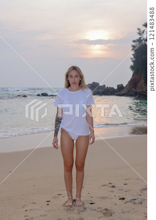 A stylish woman in a white tee shirt enjoys a vibrant sunset at the beach, soaking in the moment A stylish woman in a white tee shirt enjoys a vibrant sunset at the beach, soaking in the moment 121483488