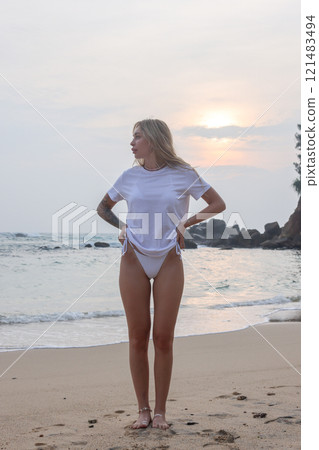 A stylish woman in a white tee shirt enjoys a vibrant sunset at the beach, soaking in the moment A stylish woman in a white tee shirt enjoys a vibrant sunset at the beach, soaking in the moment 121483494