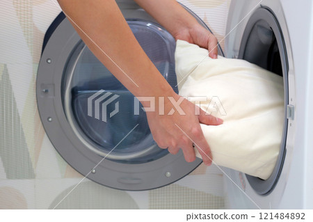 Man's hand holds a pillow and puts it in the washing machine. Man's hand holds a pillow and puts it in the washing machine. 121484892