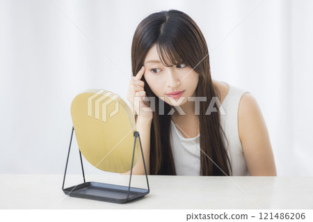 A young woman looks in the mirror and worries about her skin 121486206