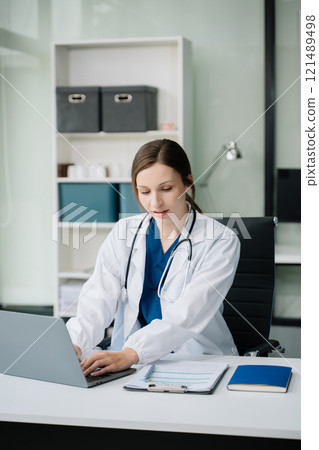 Young female doctor in white medical uniform using laptop and tablet talking video conference call at desk,Doctor sitting at desk Young female doctor in white medical uniform using laptop and tablet talking video conference call at desk,Doctor sitting at desk 121489498