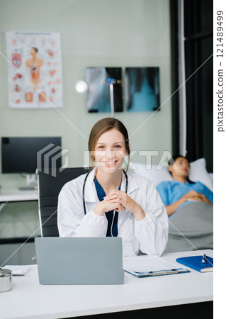 Young female doctor in white medical uniform using laptop and tablet talking video conference call at desk,Doctor sitting at desk Young female doctor in white medical uniform using laptop and tablet talking video conference call at desk,Doctor sitting at desk 121489499
