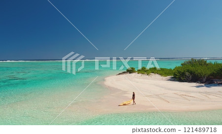 Aerial view of woman pulling kayak on turquoise lagoon beach in the tropics, creating a serene oasis for a relaxing vacation in paradise 121489718