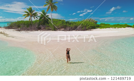 Beautiful woman enjoying tropical holidays on a secluded island with crystal-clear waters and white sands, creating a serene and luxurious vacation moment 121489719