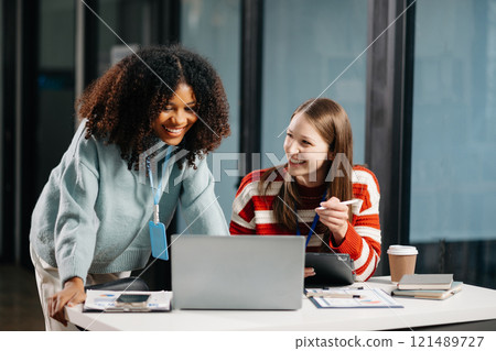 Businesswomen work and discuss their business plans. African women employee explains and shows her colleague the results paper in modern office. 121489727
