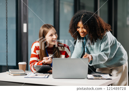 Businesswomen work and discuss their business plans. African women employee explains and shows her colleague the results paper in modern office. 121489728