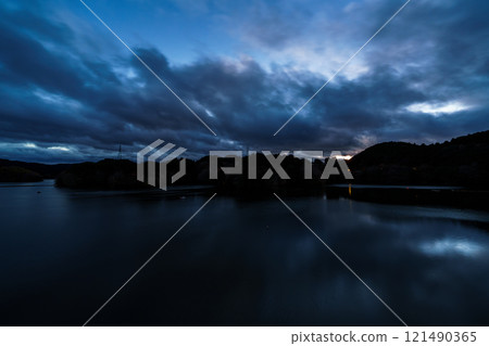 Midwinter at Nunome Dam. The evening sky from sunset to blue hour and beautiful reflections on the lake surface. 121490365