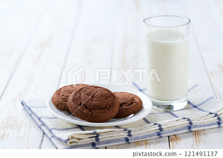 Tasty chocolate cookies and glass milk on a light kitchen table, selective focus. Tasty chocolate cookies and glass milk on a light kitchen table, selective focus. 121491137