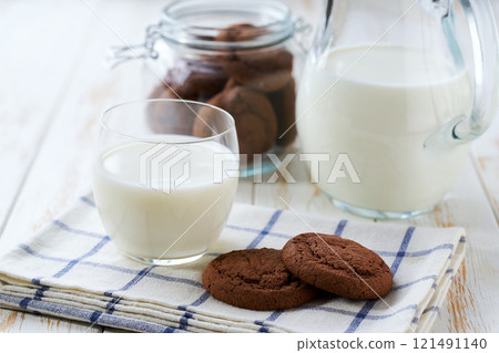 Glass and a jug of fresh milk with delicious chocolate brownie cookies on a white table, selective focus. 121491140