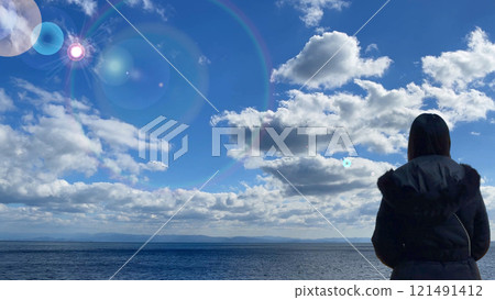 The back view of a young woman looking out over the refreshing blue sky and sea with sunlight sparkling The back view of a young woman looking out over the refreshing blue sky and sea with sunlight sparkling 121491412