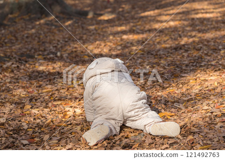 [One-year-old child sitting and playing in a winter park covered with fallen leaves] 121492763