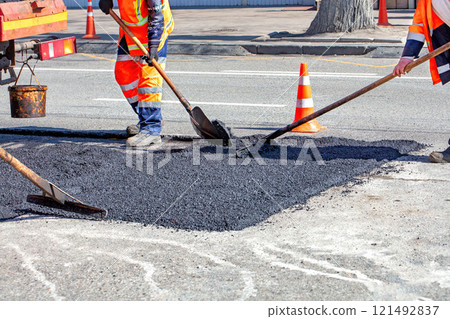 Road workers repair pavement on a sunny day with bright orange cones marking the site Road workers repair pavement on a sunny day with bright orange cones marking the site 121492837