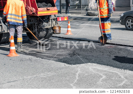 Road workers repair asphalt surface during bright day in urban setting 121492838