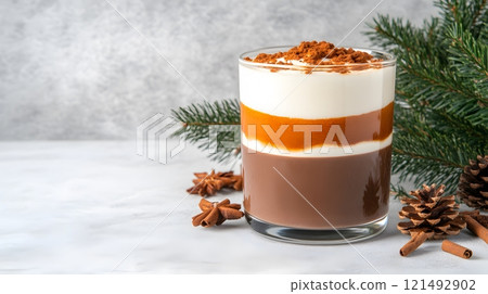 Warm hot chocolate in a clear glass mug, layered with cream and chocolate syrup, festive atmosphere 121492902