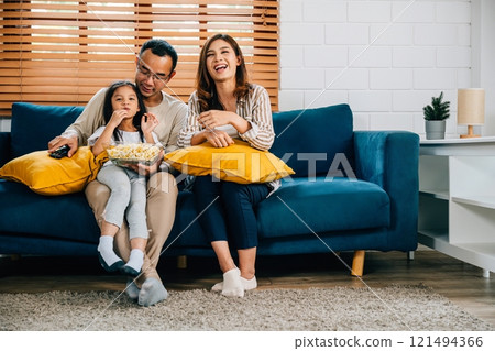 In their cozy house family enjoys quality time together watching a video with popcorn. father mother son daughter and schoolgirl are all smiles fostering togetherness and happiness. In their cozy house family enjoys quality time together watching a video with popcorn. father mother son daughter and schoolgirl are all smiles fostering togetherness and happiness. 121494366