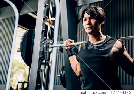 Asian muscular man guy performing a squat exercise legs heavy weights with a barbell in gym, men doing lifting barbell work out at fitness gym, sport workout healthy lifestyle concept 121494380