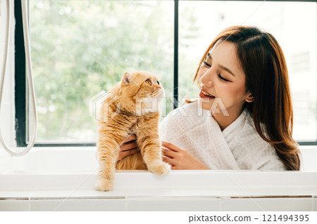 A clean and happy moment in the bathroom, a woman and her Scottish Fold cat enjoy bath time together, a scene of pure owner-pet love. A clean and happy moment in the bathroom, a woman and her Scottish Fold cat enjoy bath time together, a scene of pure owner-pet love. 121494395
