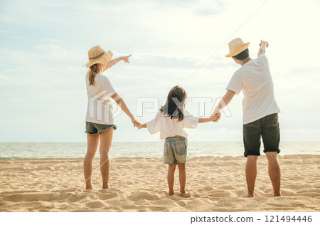 Happy Asian parents with their daughters enjoying playful at beach. Little girls with their mother and father holding hand of child walking on sand beach. Positive family outdoor activity 121494446
