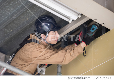 A person in work clothes wearing a safety harness making repairs using scaffolding 121494677