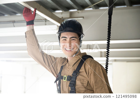 一個穿著工作服、繫著安全帶、對著鏡頭微笑的年輕人 一個穿著工作服、繫著安全帶、對著鏡頭微笑的年輕人 121495098