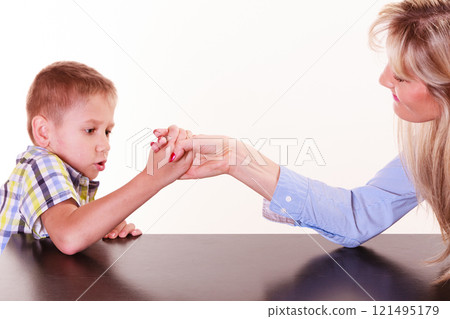 Mother and son arm wrestle sit at table. 121495179
