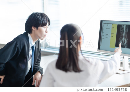 A middle-aged female doctor and a patient examining a patient while looking at an X-ray of the lower back 121495738