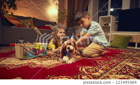 Boy and girl playing with dog in cozy living room, using toy medical tools to pretend they are veterinarians. Warm-lit living room Boy and girl playing with dog in cozy living room, using toy medical tools to pretend they are veterinarians. Warm-lit living room 121495864
