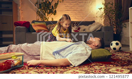 Young girl playing with her father, pretending to be a doctor, using stethoscope. Cute family moment in cozy living room at home in the evening Young girl playing with her father, pretending to be a doctor, using stethoscope. Cute family moment in cozy living room at home in the evening 121495877