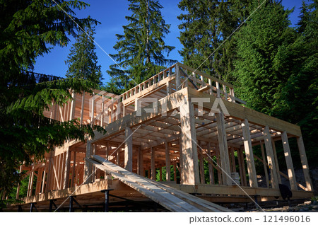 Residential building with wooden frame in process of being built near a forest. Beginning of new construction of comfortable cottage. Idea of ecological construction, contemporary architectural design 121496016