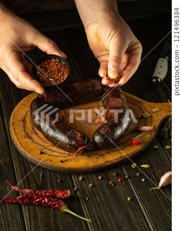 Expert hands prepare a delicious recipe while showcasing plump sausages and vibrant spices on a rustic wooden board. The atmosphere is rich with culinary tradition and flavor 121496384