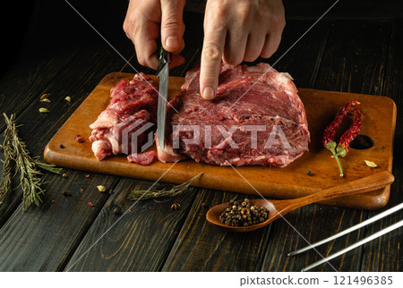 Skillful hands expertly slice fresh meat on a wooden cutting board in a rustic kitchen 121496385