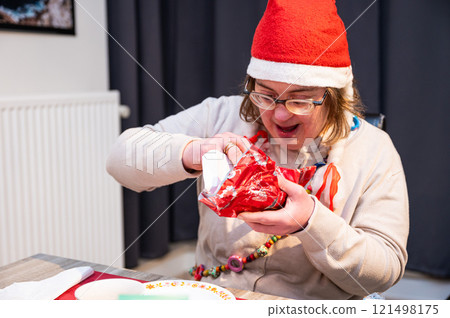 42 yo Down Syndrome woman unwrapping presents during a cosy Christmas night at home, Belgium 121498175