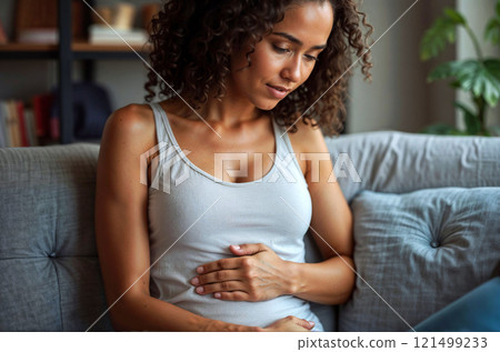 A woman is sitting on a couch with her hand on her stomach 121499233