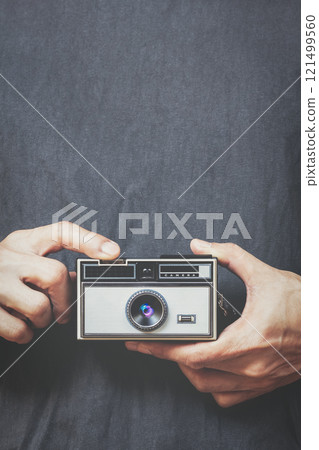 close up male hands holding retro camera and pressing shutter button on black shirt background 121499560