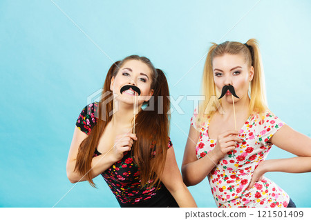 Two happy women holding fake moustache on stick 121501409