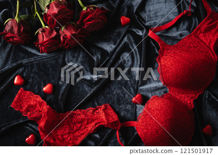 Romantic dating. Valentine's day, lace women's red underwear, lingerie, chocolate candy sweets and red roses on dark bedclothes. View from above. Copy space. 121501917